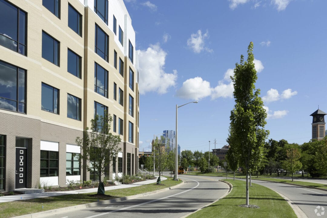 Modern building beside tree-lined street on sunny day.