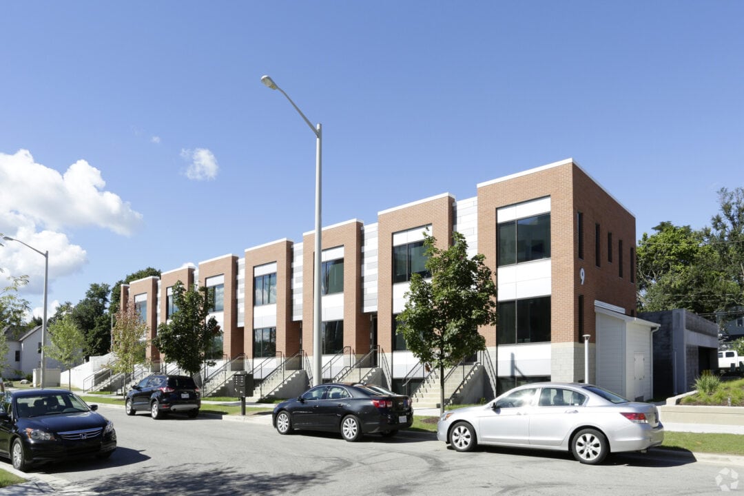 Modern townhouses on sunny street with parked cars.