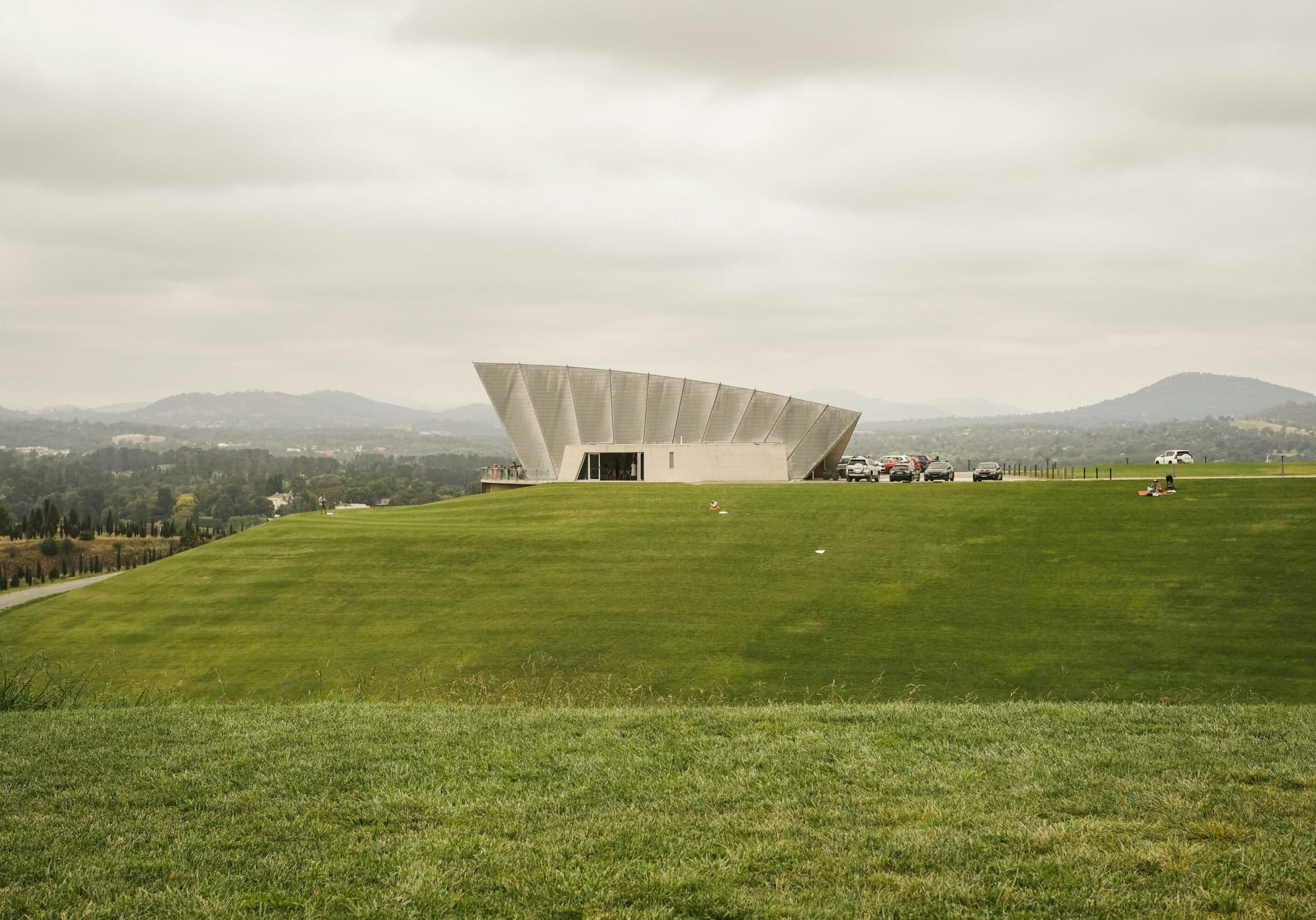 Modern building on green hill with mountains background.