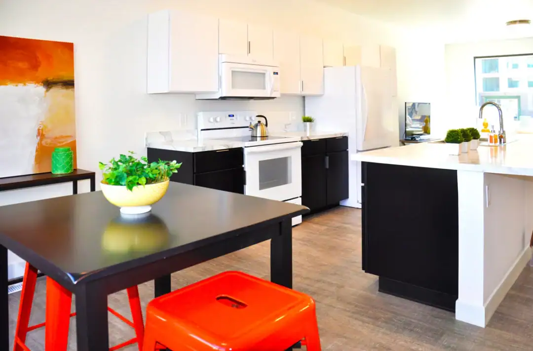 Modern kitchen with black, white cabinets, orange stool.